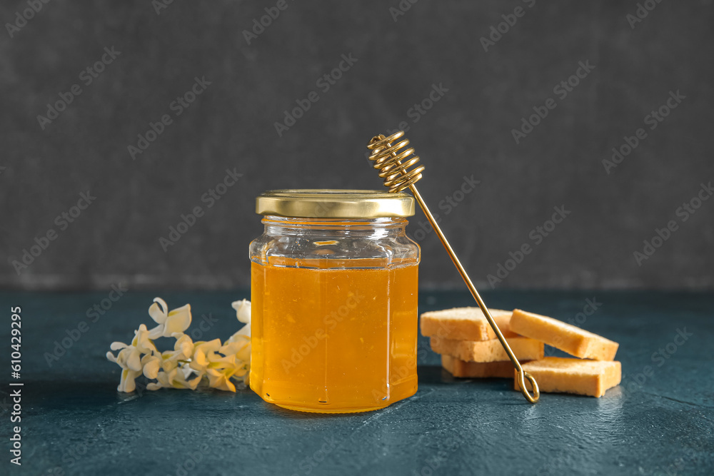 Jar of honey with flowers of acacia and crackers on dark background