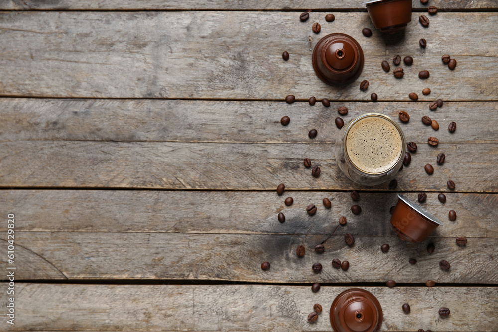 Glass of delicious coffee, pods and beans on wooden table