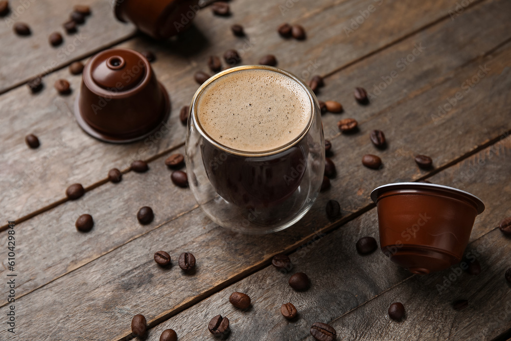 Glass of delicious coffee, pods and beans on wooden table