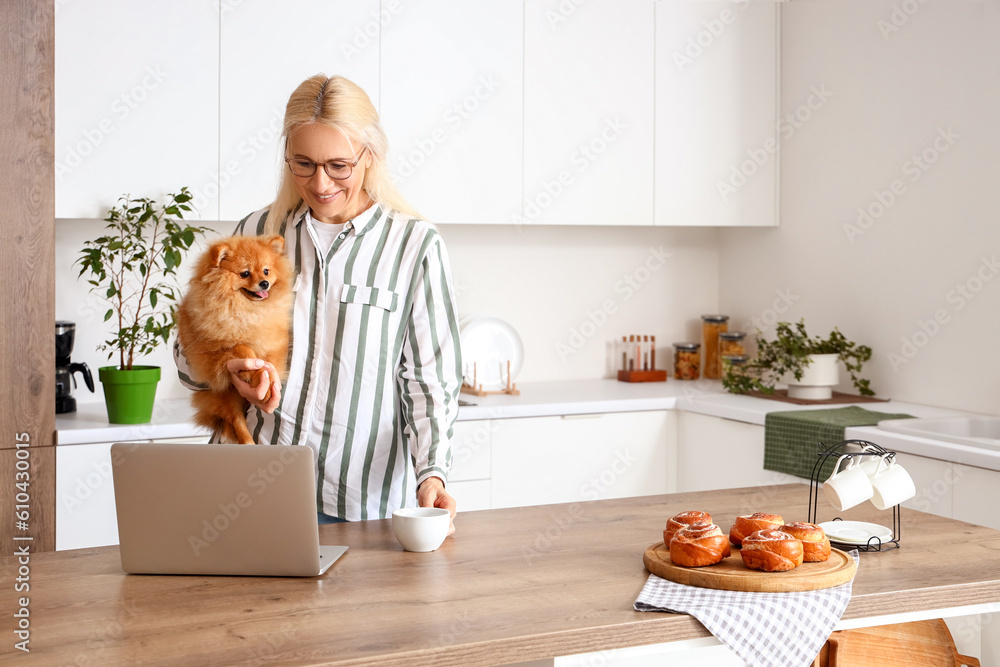 Mature woman with Pomeranian dog and cup of coffee in kitchen