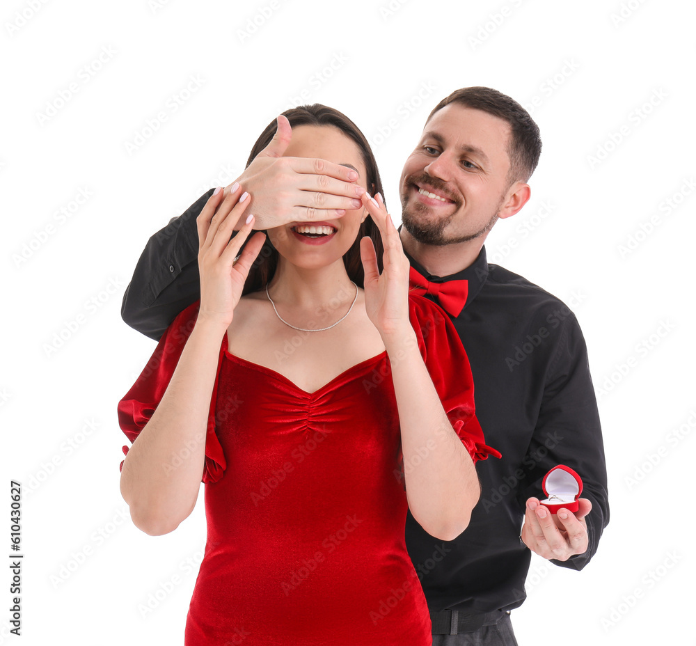 Young man with engagement ring closing his girlfriends eyes on white background