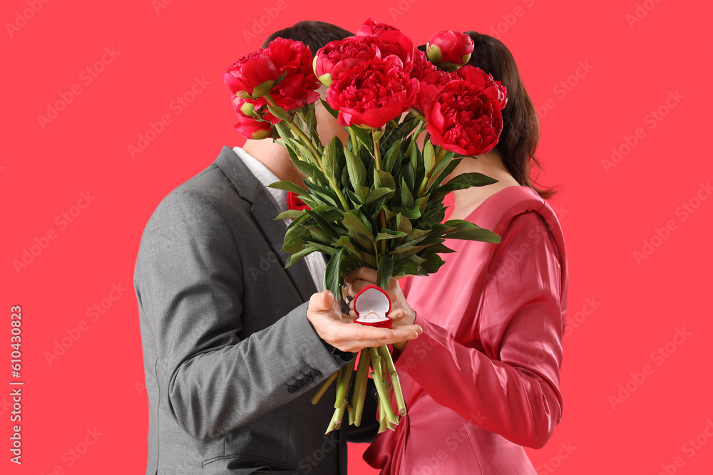 Young couple with engagement ring and flowers on red background