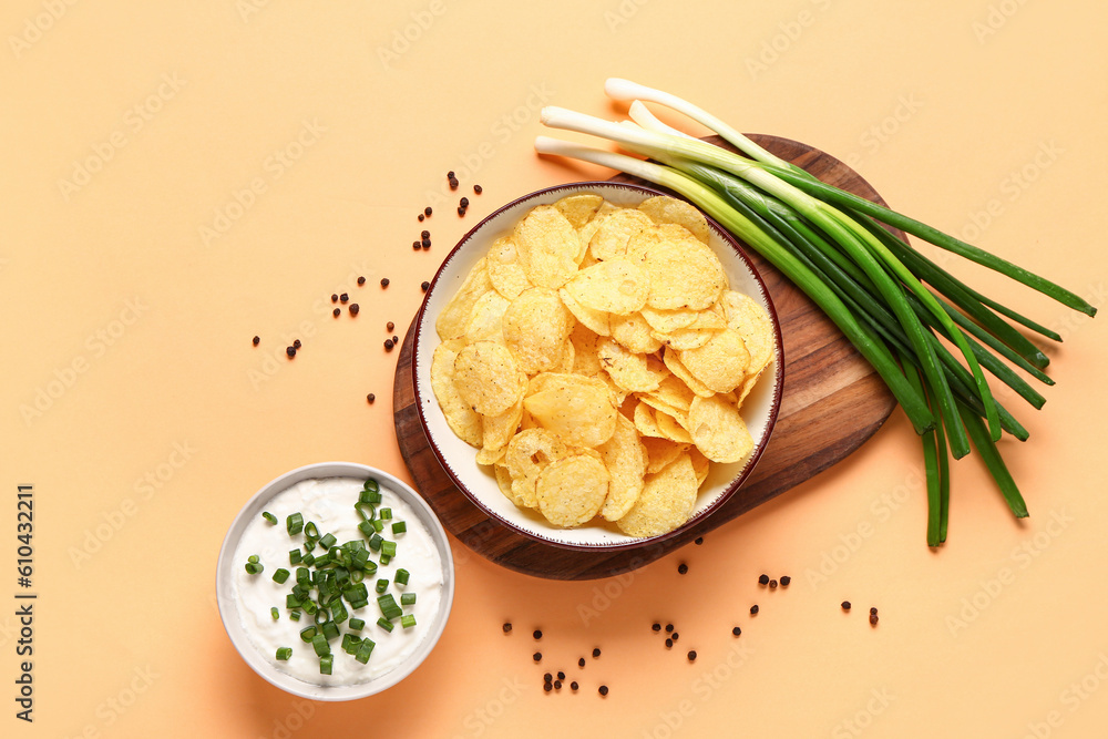 Bowl of tasty sour cream with sliced green onion and potato chips on orange background