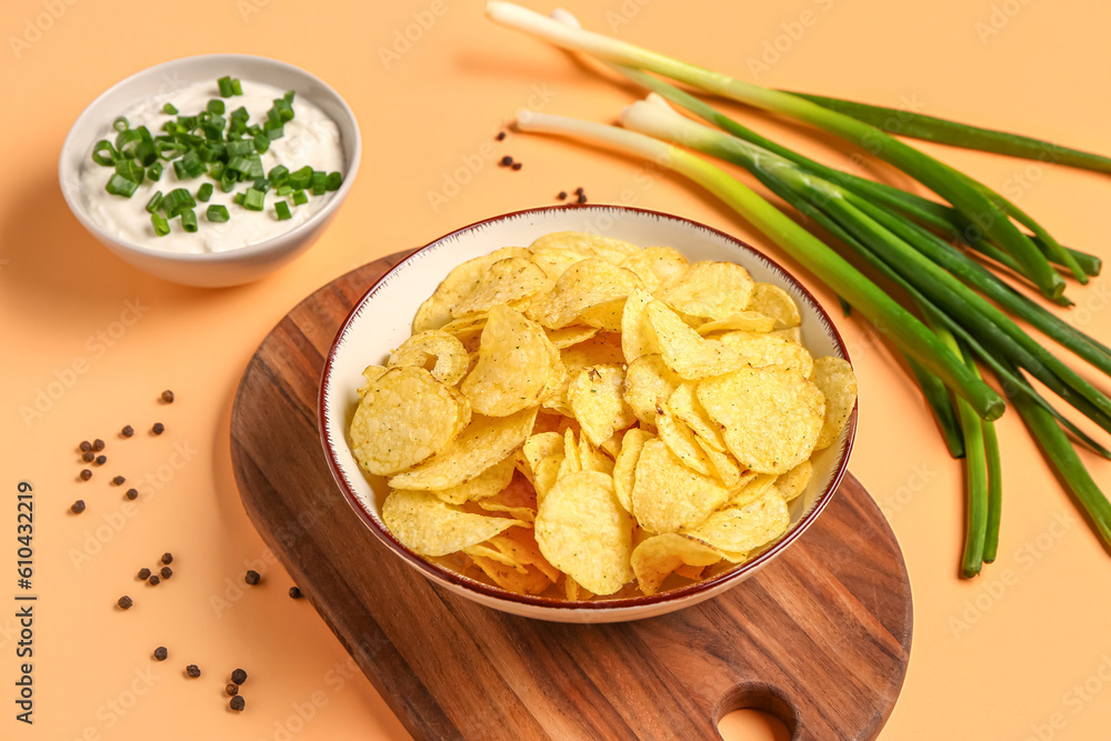 Bowl of tasty sour cream with sliced green onion and potato chips on orange background