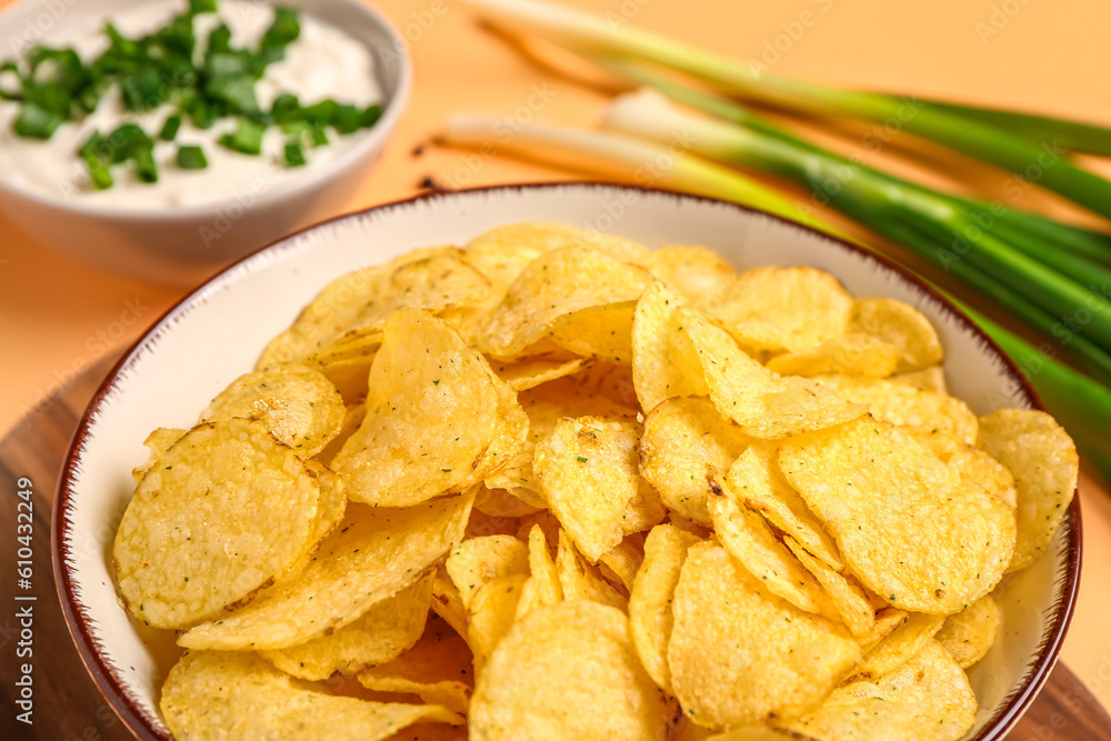 Bowl of tasty sour cream with sliced green onion and potato chips on orange background