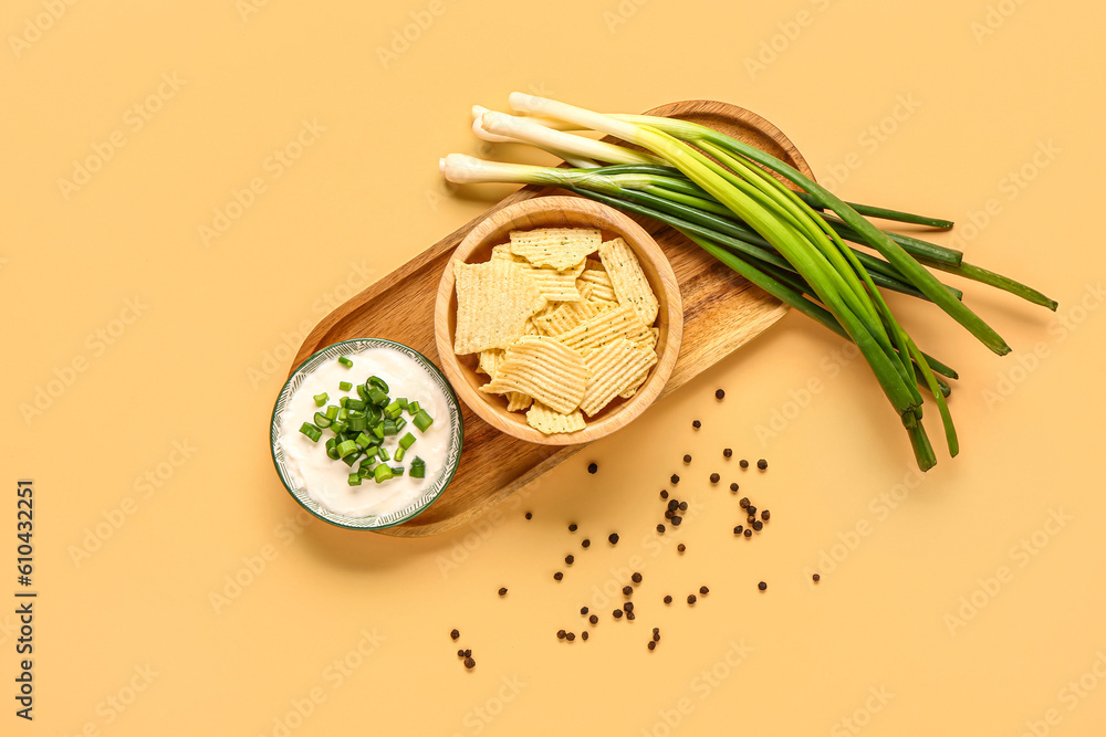 Bowl of tasty sour cream with sliced green onion and potato chips on orange background