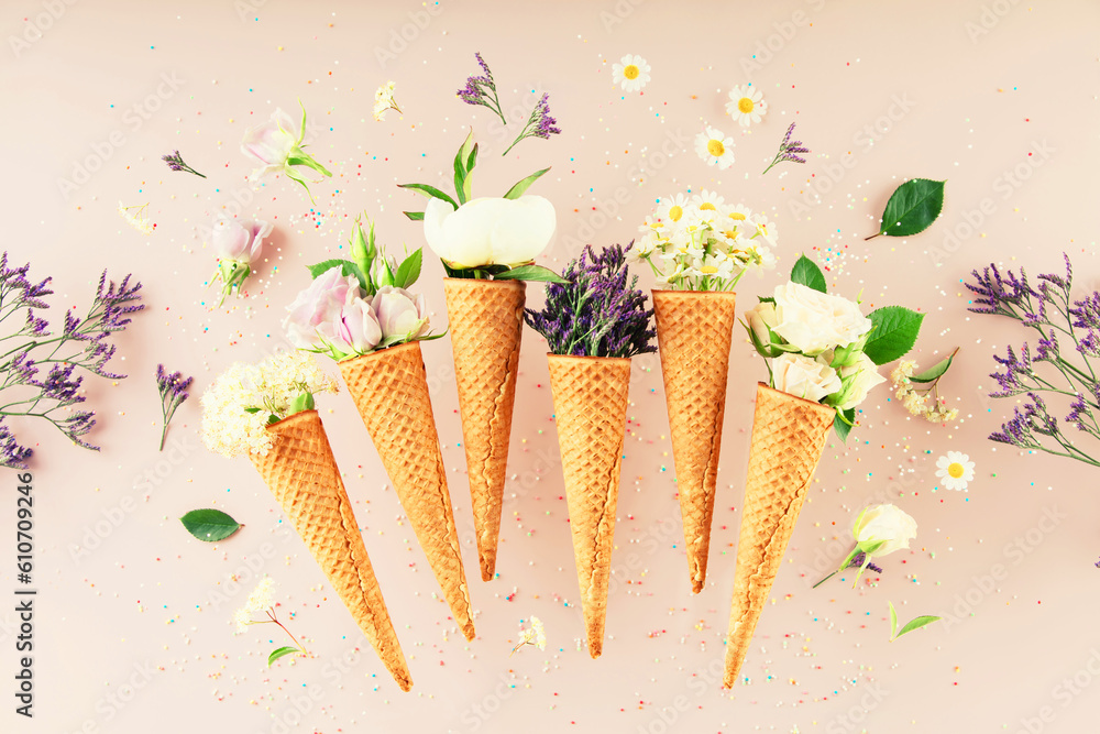 Flat-lay of waffle cones with flowers over pastel light pink background, top view