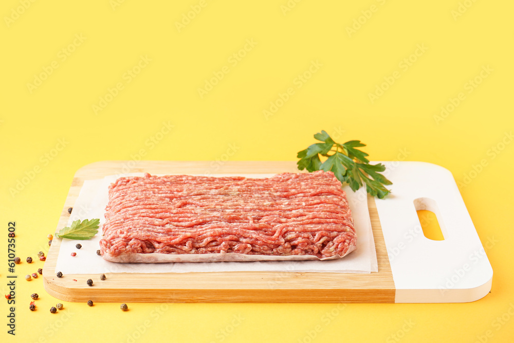 Board with fresh minced meat, parsley and peppercorns on yellow background