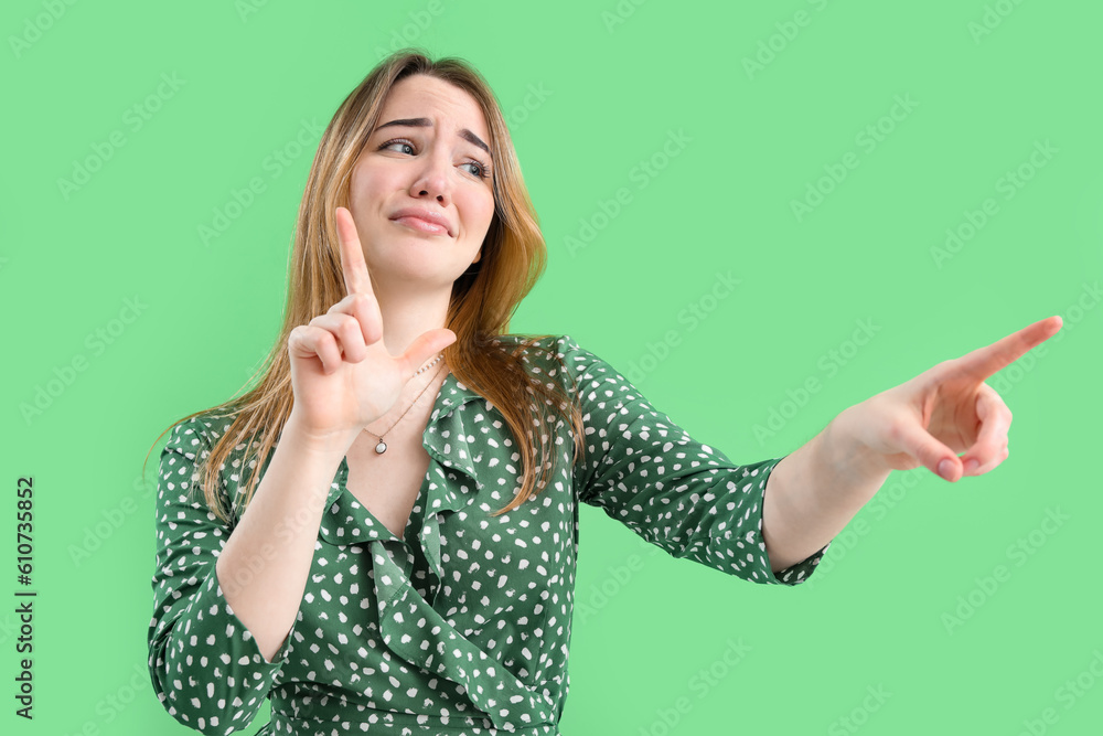 Young woman showing loser gesture on green background