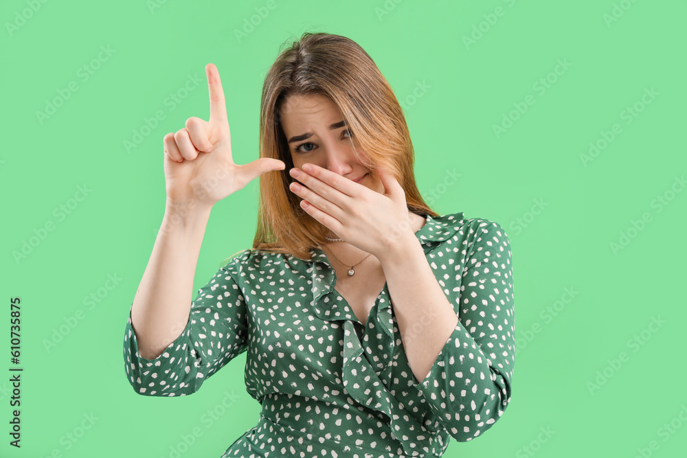 Young woman showing loser gesture on green background