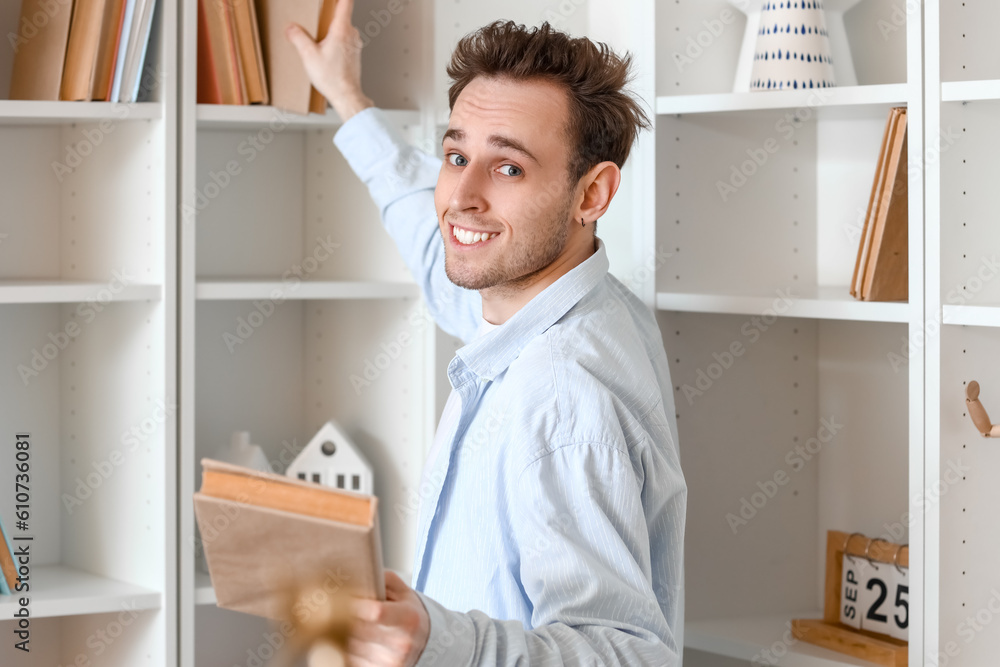 Young man taking books from shelf at home