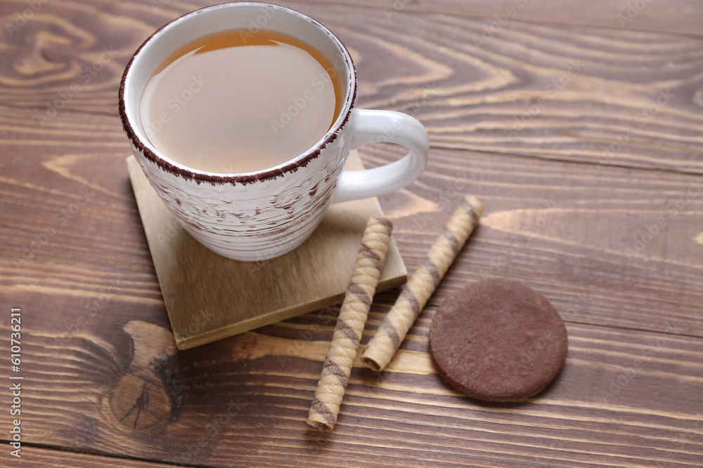 Drink coaster with cup of tea, wafer rolls and cookie on wooden table