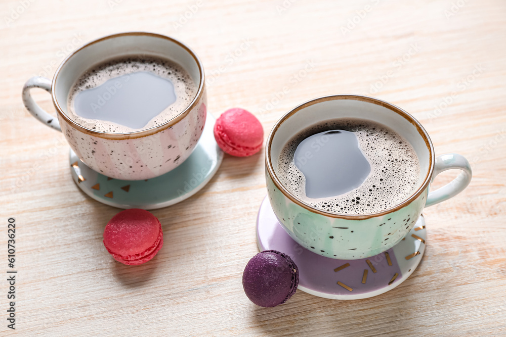 Drink coasters with cups of coffee and macaroons on wooden table