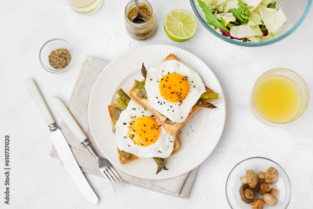 Delicious sandwiches with fried eggs and asparagus on light background