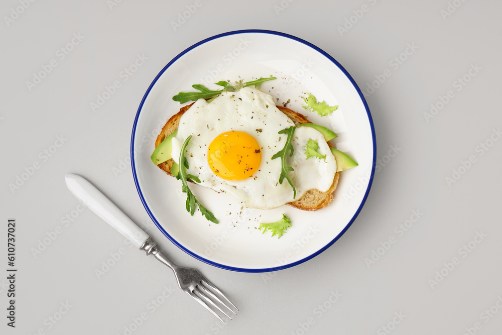 Delicious sandwich with fried egg, avocado and arugula on grey background