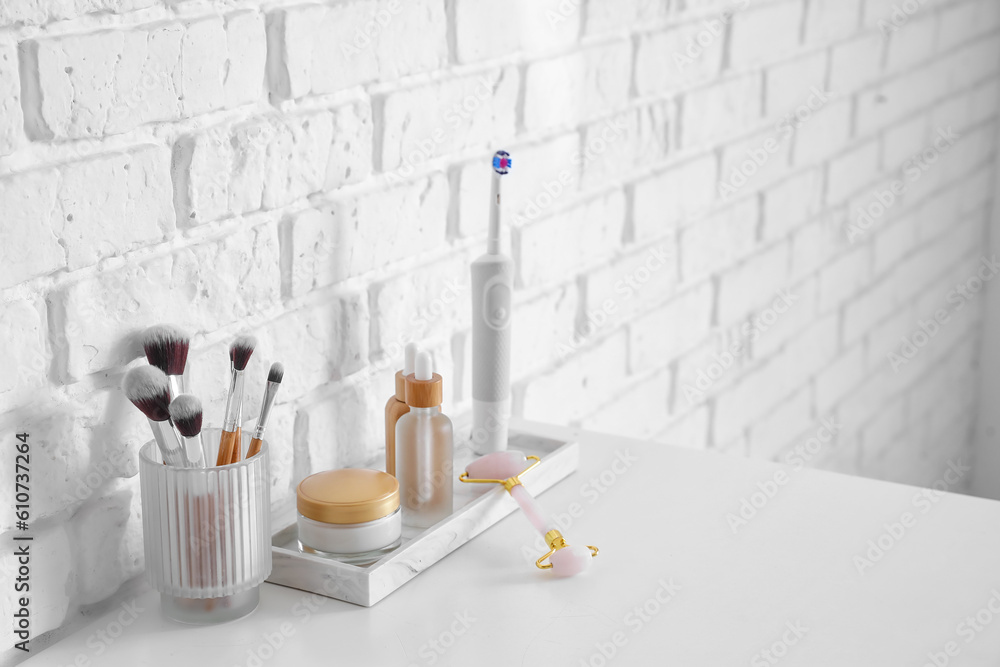 Bath accessories with makeup brushes on table near white brick wall