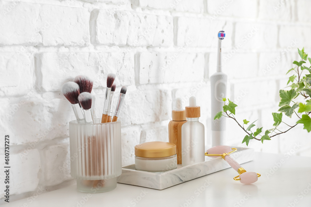 Bath accessories with makeup brushes on table near white brick wall