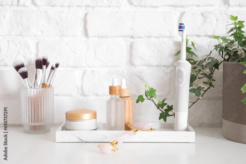 Bath accessories with makeup brushes on table near white brick wall