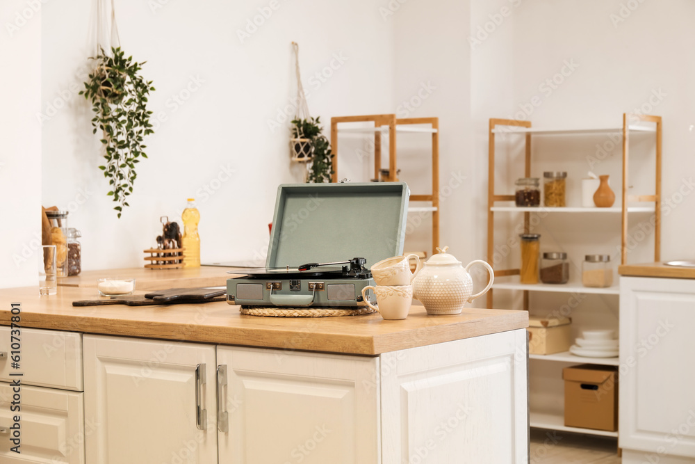 Record player with vinyl disk, cups and teapot on counter in kitchen