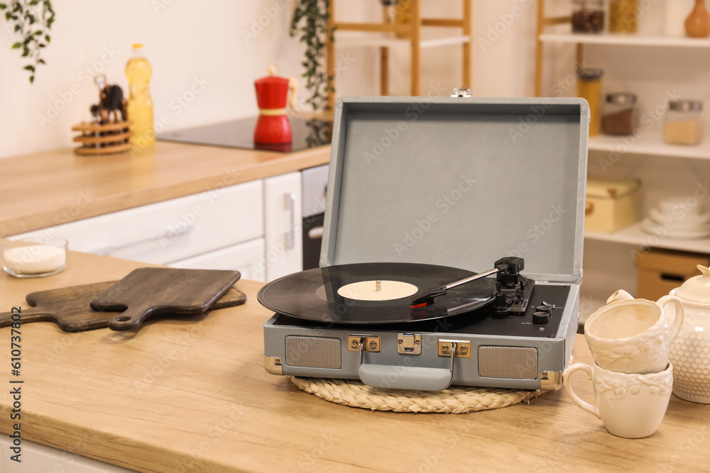 Record player with vinyl disk, cups and teapot on counter in kitchen