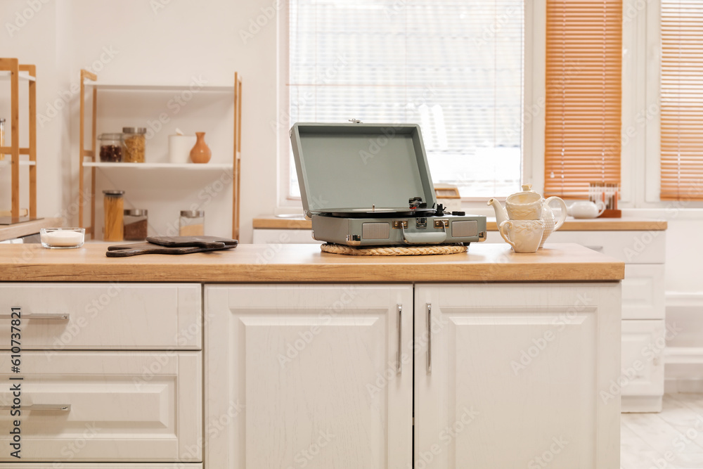 Record player with vinyl disk, cups and teapot on counter in kitchen