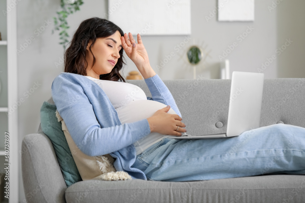 Tired young pregnant woman working with laptop on sofa at home