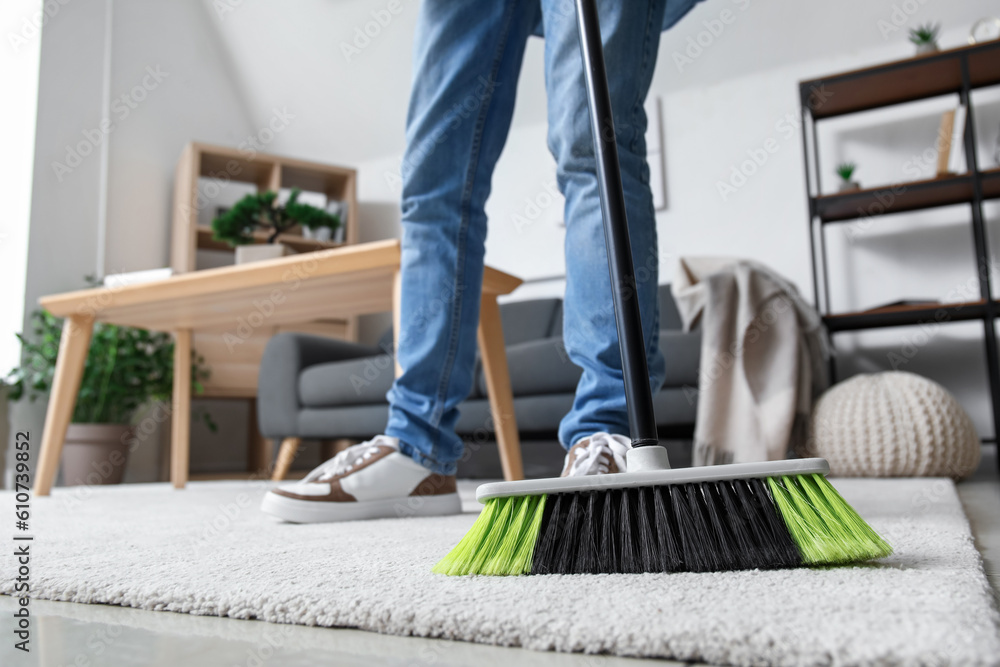 Young man sweeping carpet with broom at home, closeup