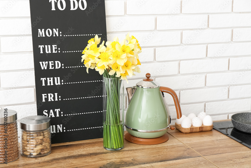 Vase with blooming narcissus flowers on counter in interior of kitchen