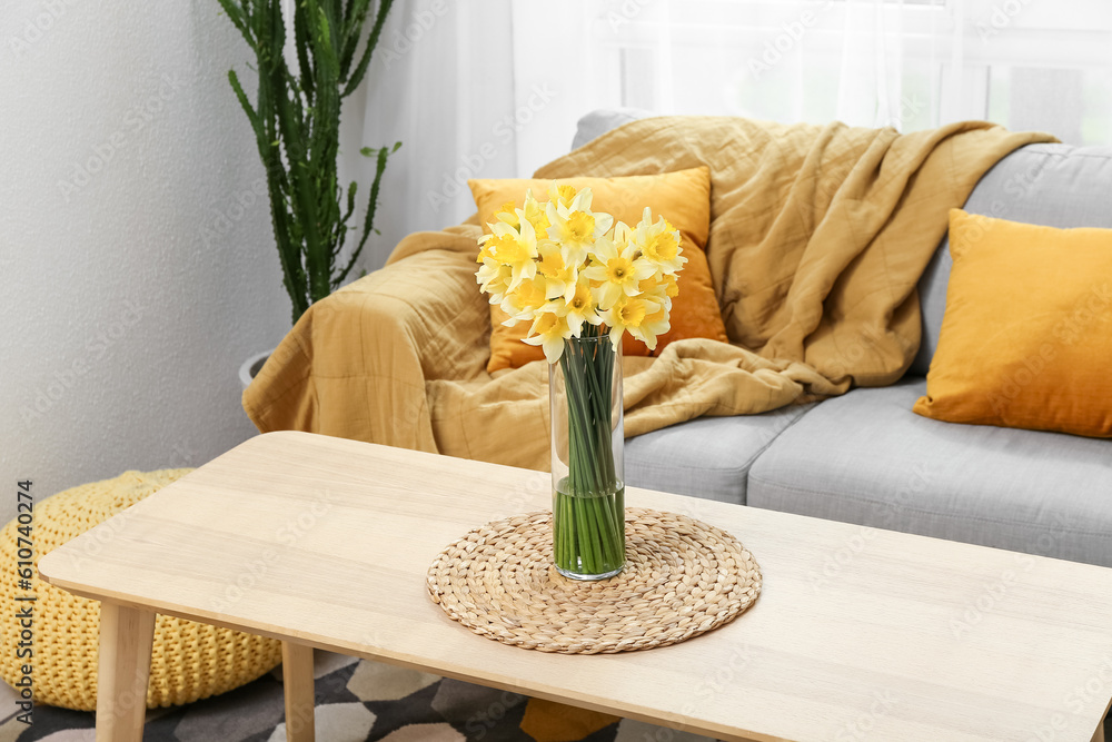 Vase with blooming narcissus flowers on table in light living room, closeup