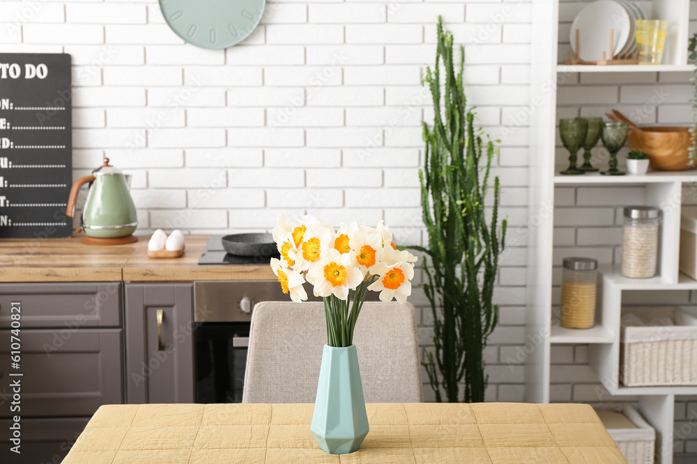 Interior of modern kitchen with blooming narcissus flowers in vase on table