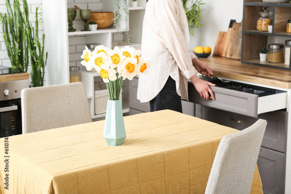 Woman cooking in modern kitchen with narcissus flowers on table