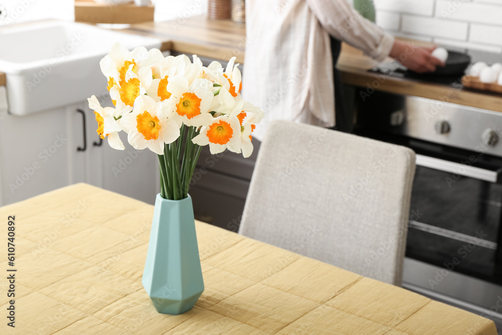 Woman cooking in modern kitchen with narcissus flowers on table