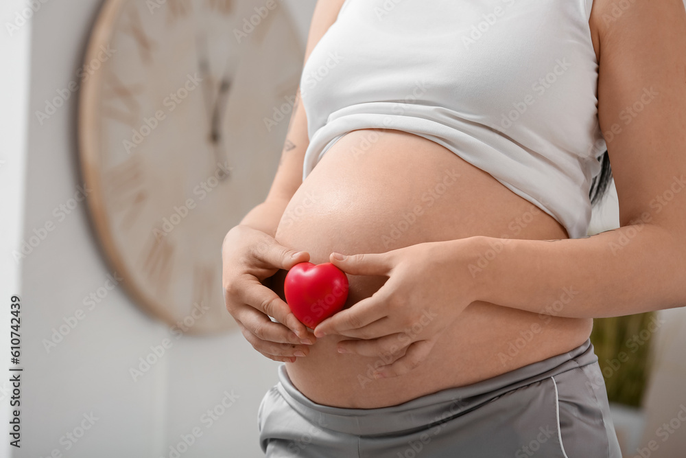 Young pregnant woman with heart in bedroom, closeup