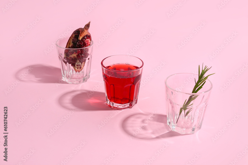 Glasses of fresh pomegranate juice and rosemary on pink background