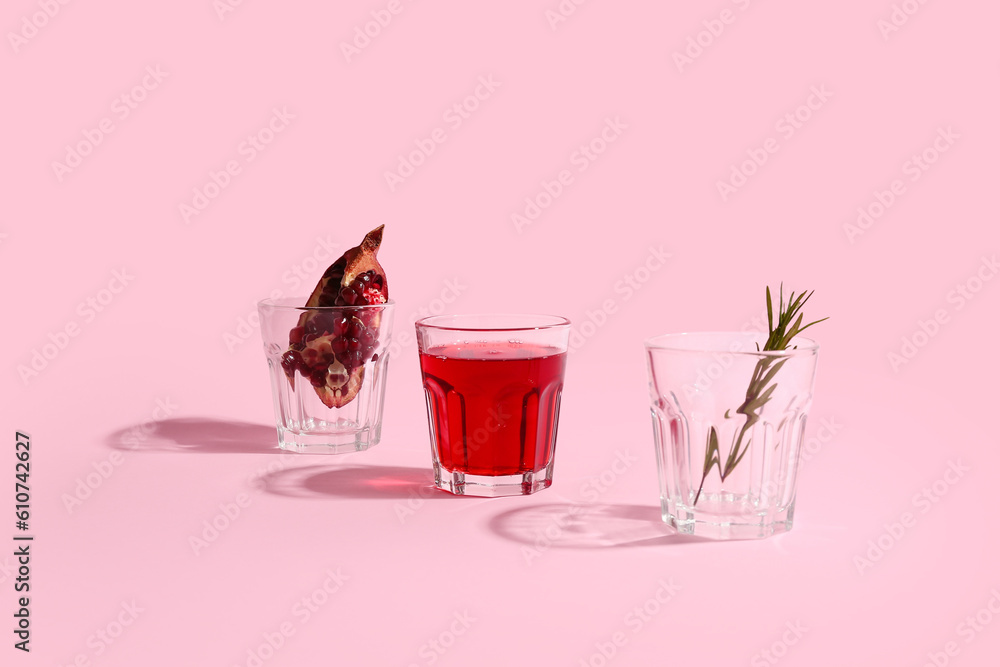 Glasses of fresh pomegranate juice and rosemary on pink background