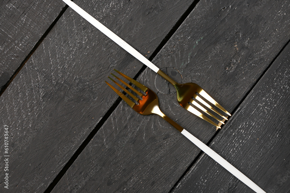 Golden forks with white handles on black wooden background