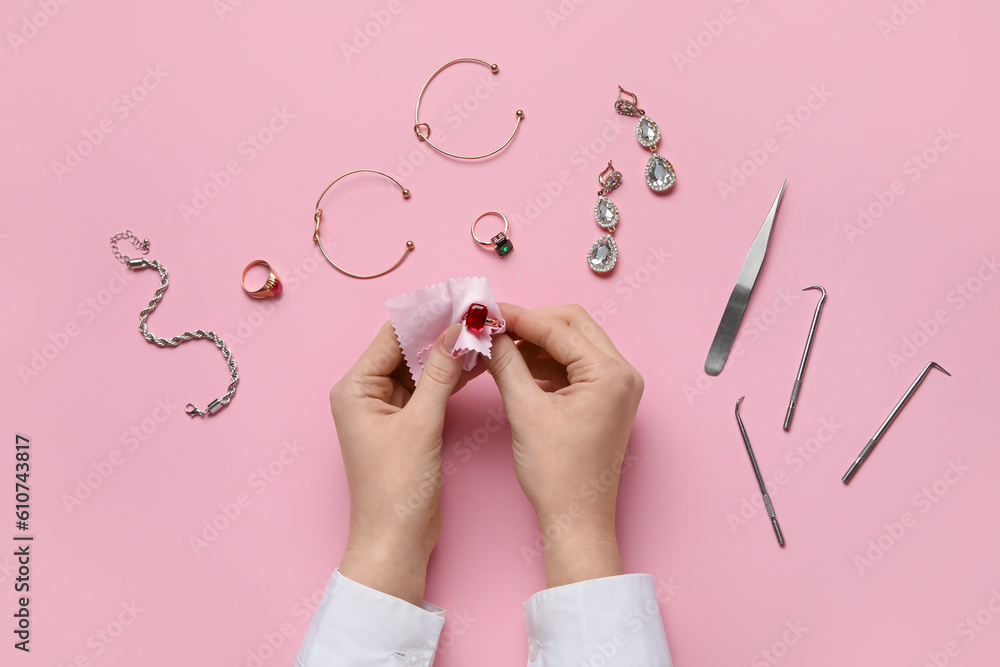 Woman cleaning beautiful jewelry on pink background