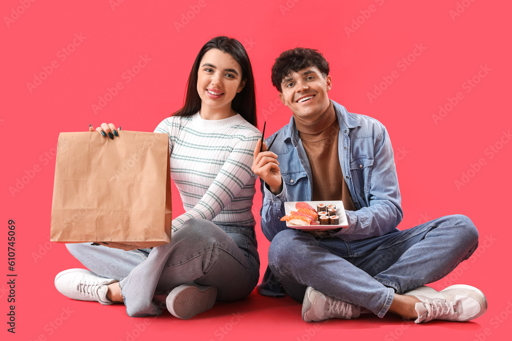 Young couple with sushi and paper bag sitting on red background