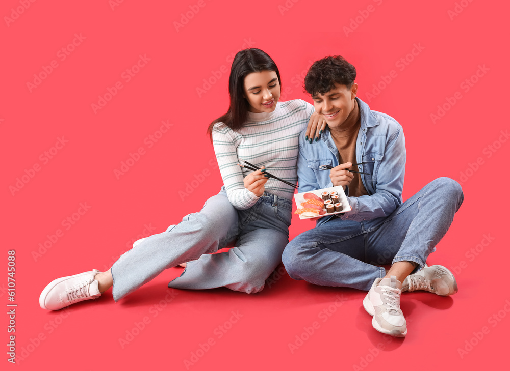 Young couple eating sushi on red background