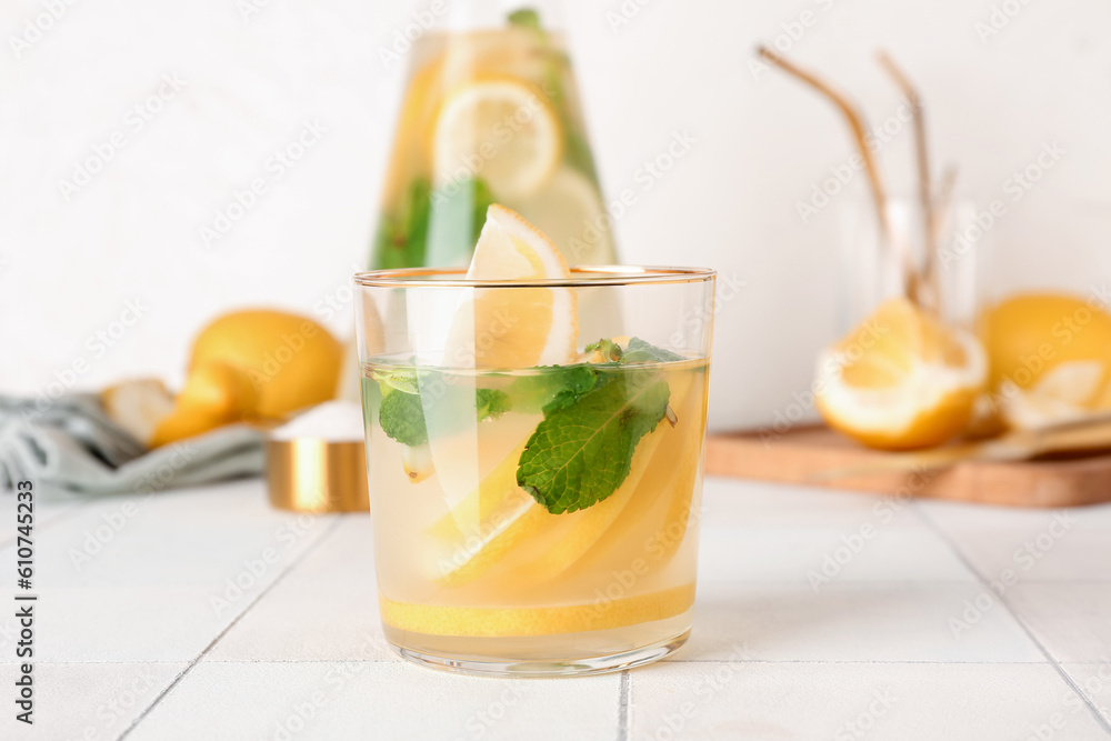 Jug and glass with fresh lemonade on white tile table