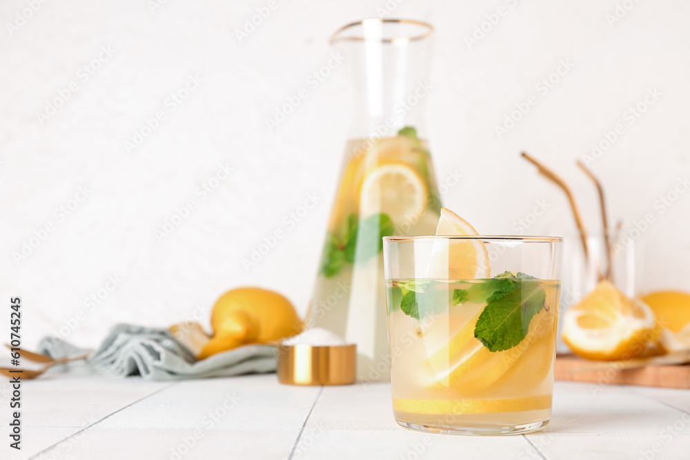 Jug and glass with fresh lemonade on white tile table