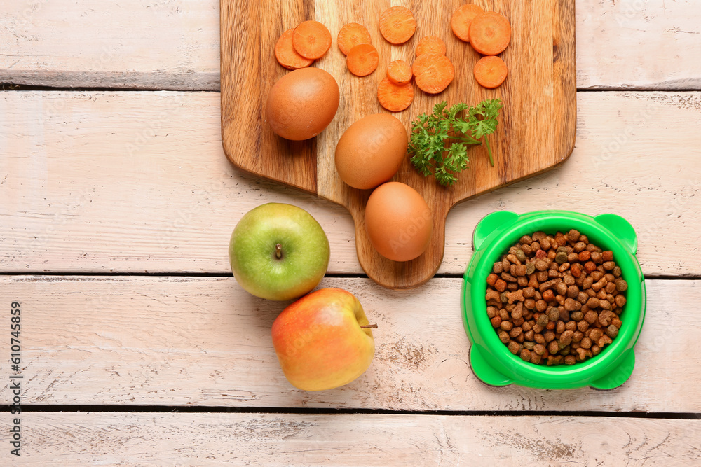 Composition with dry pet food and natural products on light wooden background