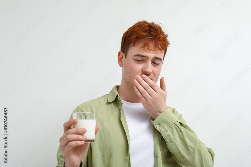 Displeased young man with glass of milk on white background