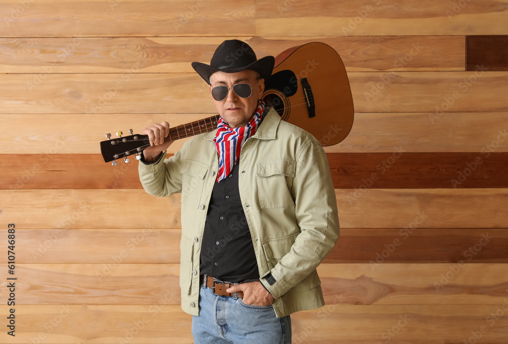 Mature cowboy with guitar on wooden background