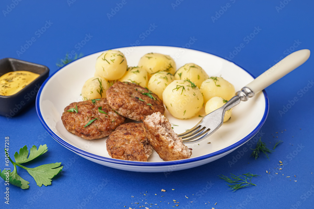 Plate with cutlets, boiled baby potatoes and dill on blue background