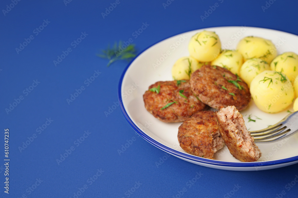 Plate with cutlets, boiled baby potatoes and dill on blue background