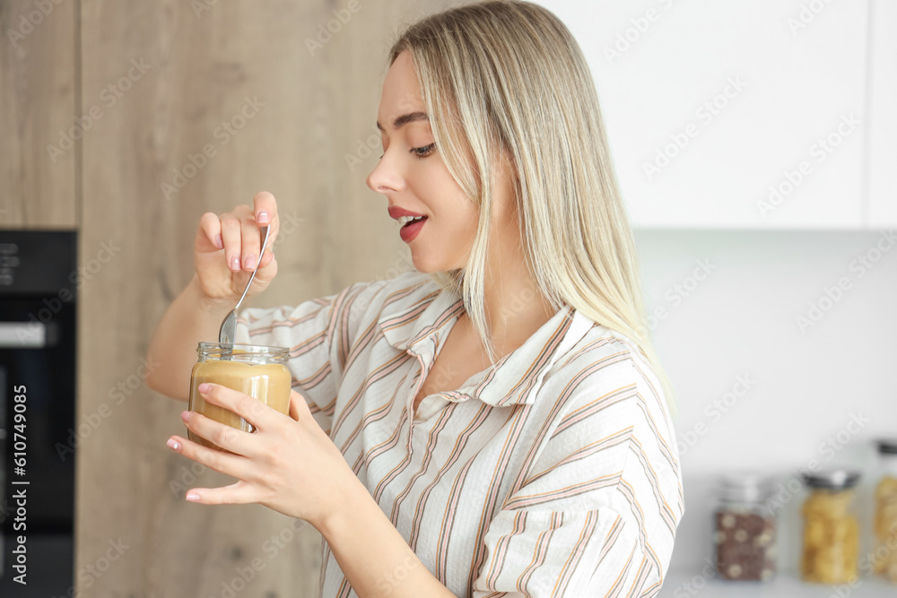 Young woman with spoon and jar of nut butter in kitchen