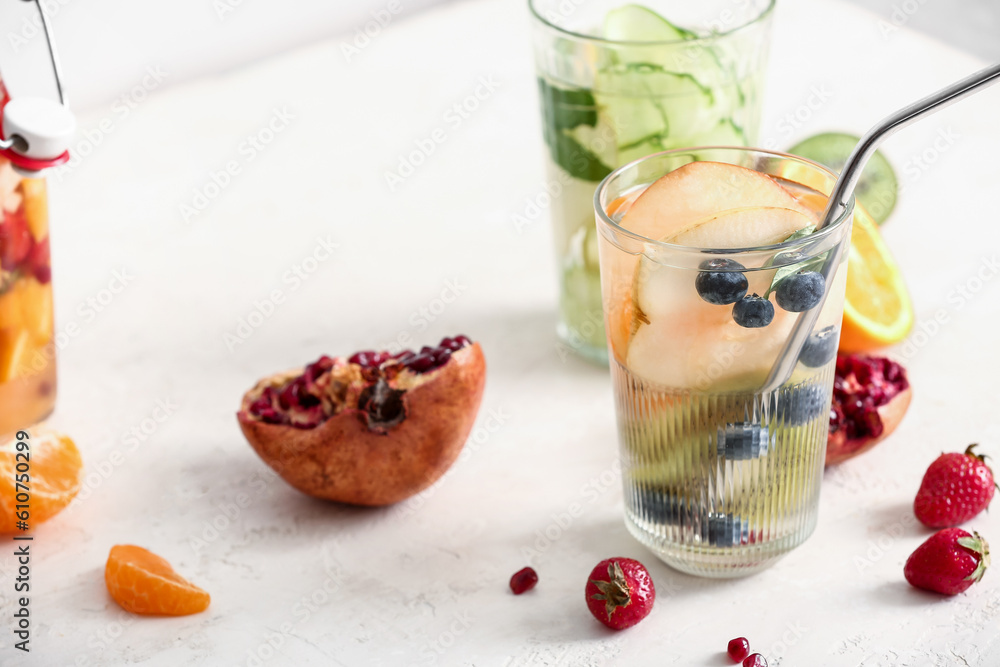 Glasses of infused water with different sliced fruits on white table