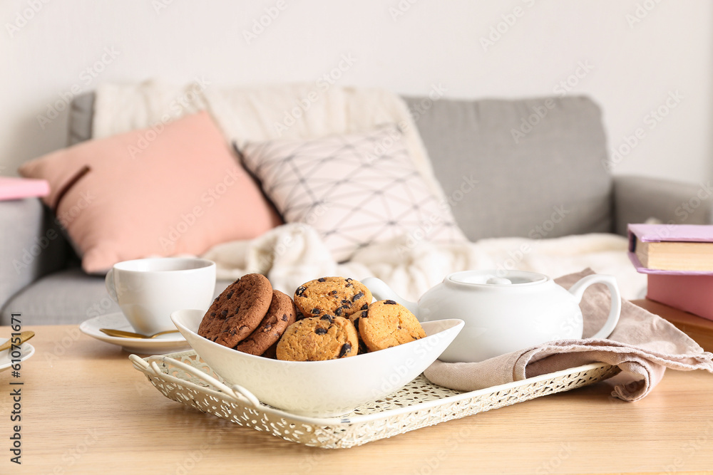 Bowl with cookies, teapot and cups of tea on wooden table in living room