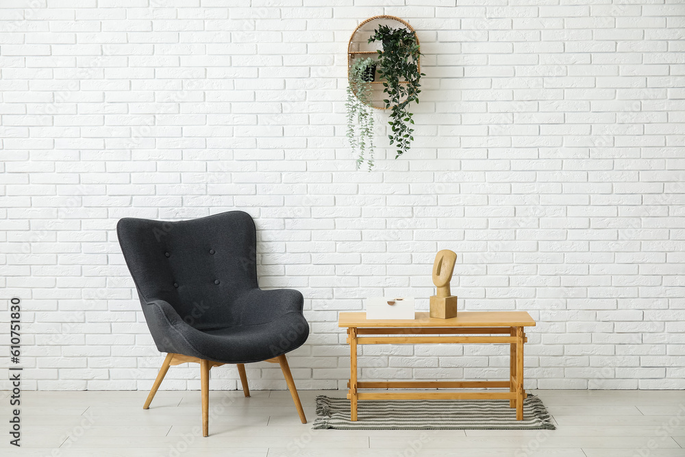 Dark grey armchair with coffee table, houseplants and rug near white brick wall